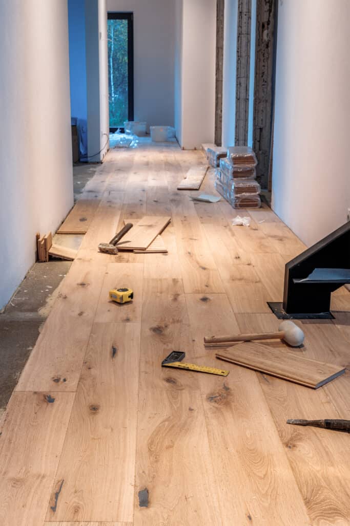 Installation de parquet en bois : rénovation du sol de maison Couloir en rénovation avec installation de parquet en bois clair. Des planches et outils (marteau, mètre) sont sur le sol.