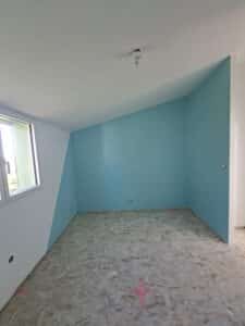Chambre mansardée avec peinture bleu turquoise, murs blancs et sol en OSB lors d'une rénovation intérieure.
