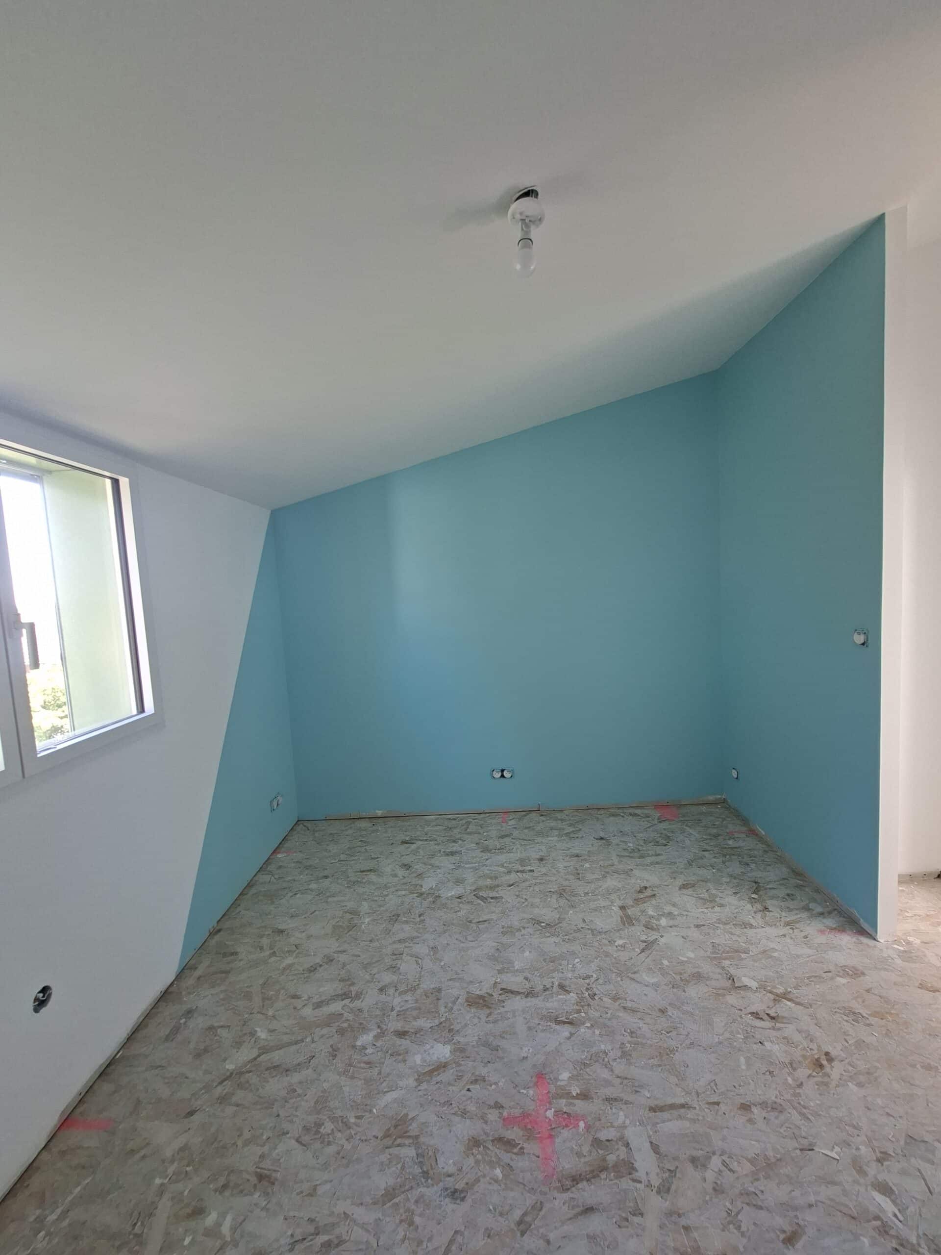 Chambre mansardée avec peinture bleu turquoise, murs blancs et sol en OSB lors d'une rénovation intérieure.